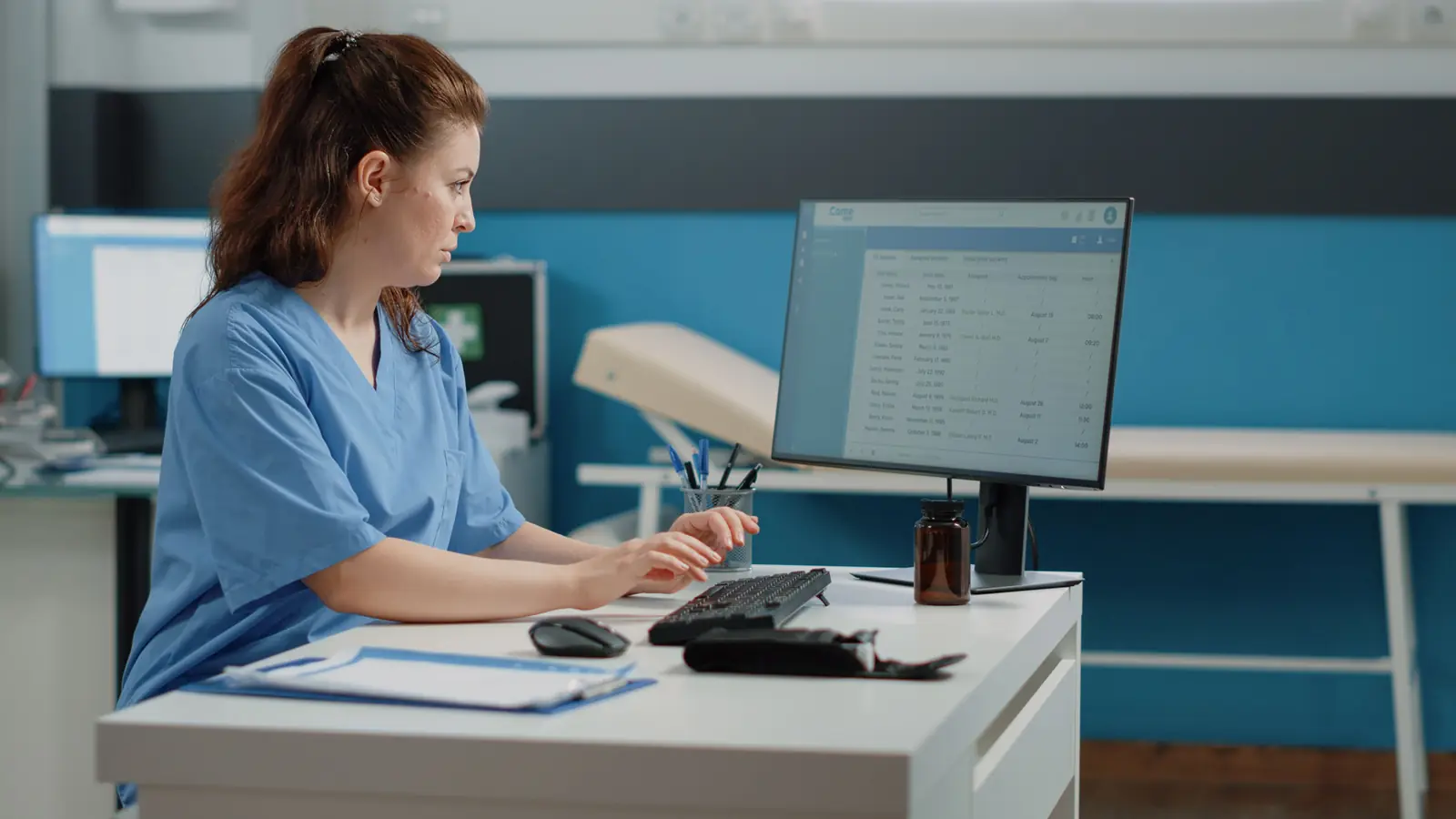 A nurse in blue scrubs working on a computer at a clinic desk