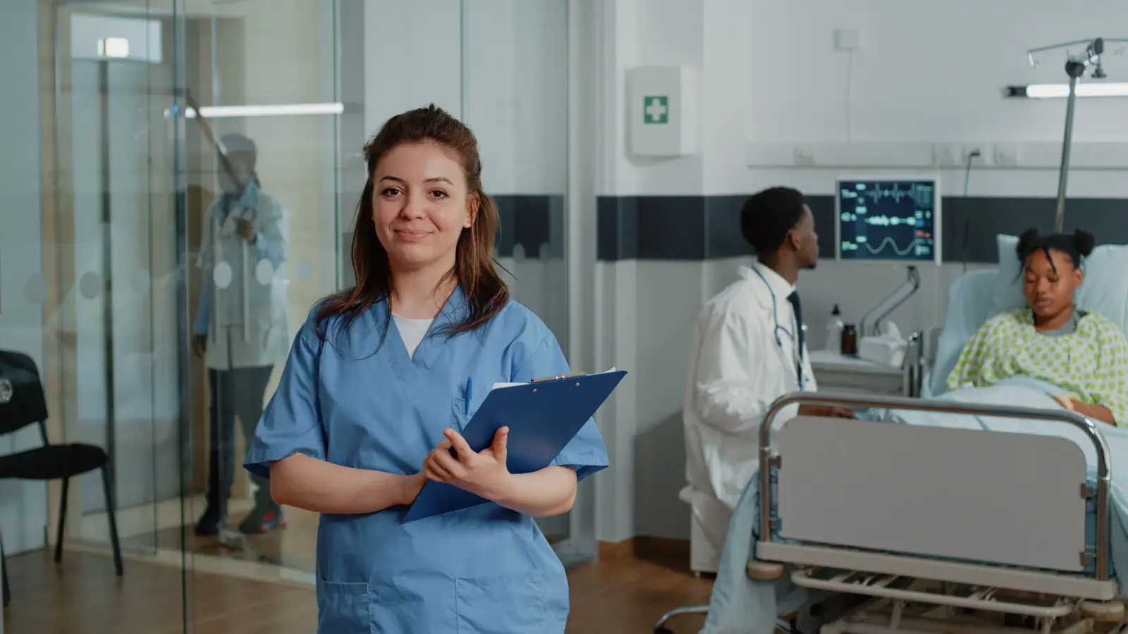 A smiling nurse holding her paperwork on a clipboard in a hospital ward