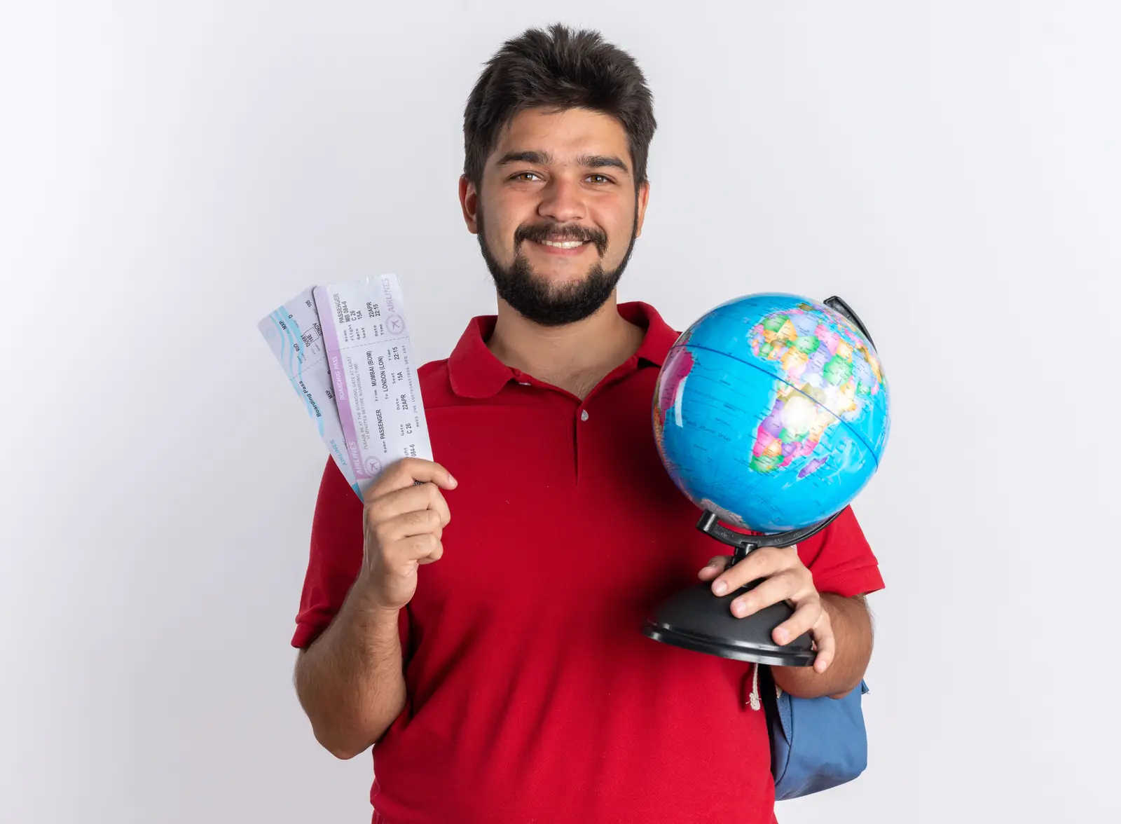 A smiling student with a backpack holding travel tickets and a globe